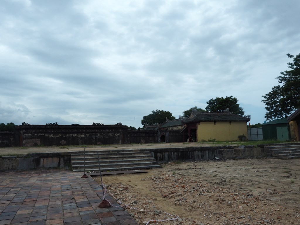 A view of the historic citadel in Hue, Vietnam, featuring stone steps and weathered brick walls under a cloudy sky.